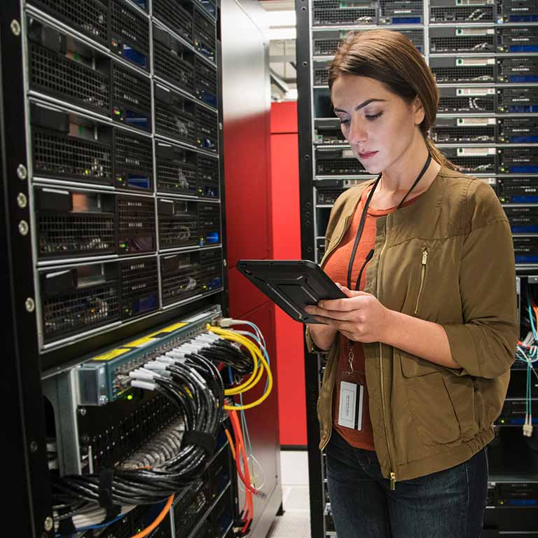 A person with a tablet checks the wiring on a rack of computers.