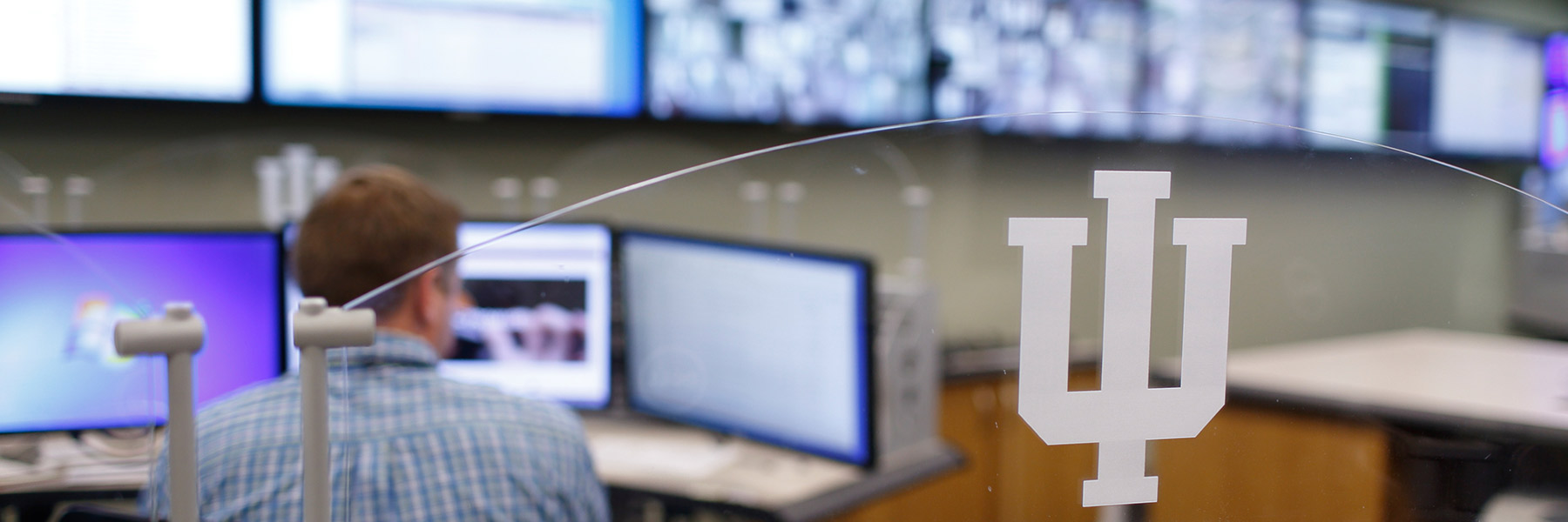 A person sits behind a glass partition marked with the IU trident.